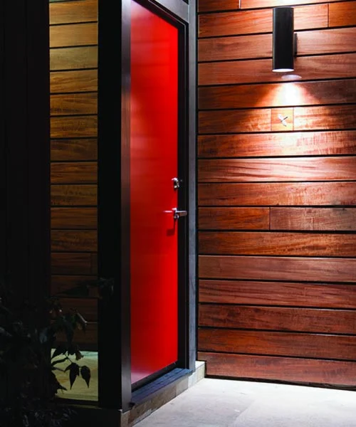 DRACO Design and Construction A red door on a wooden wall at night.