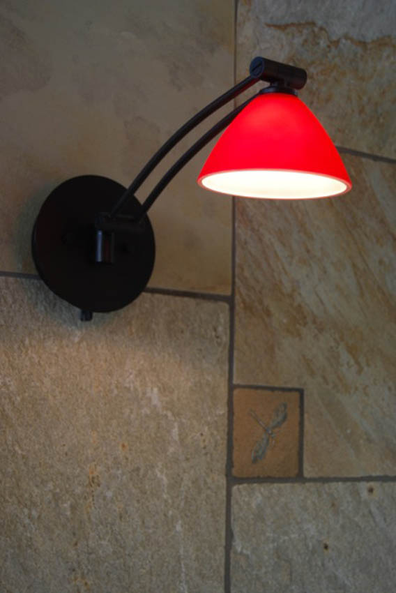 DRACO Design and Construction A wall lamp with a red glass shade on a stone wall.